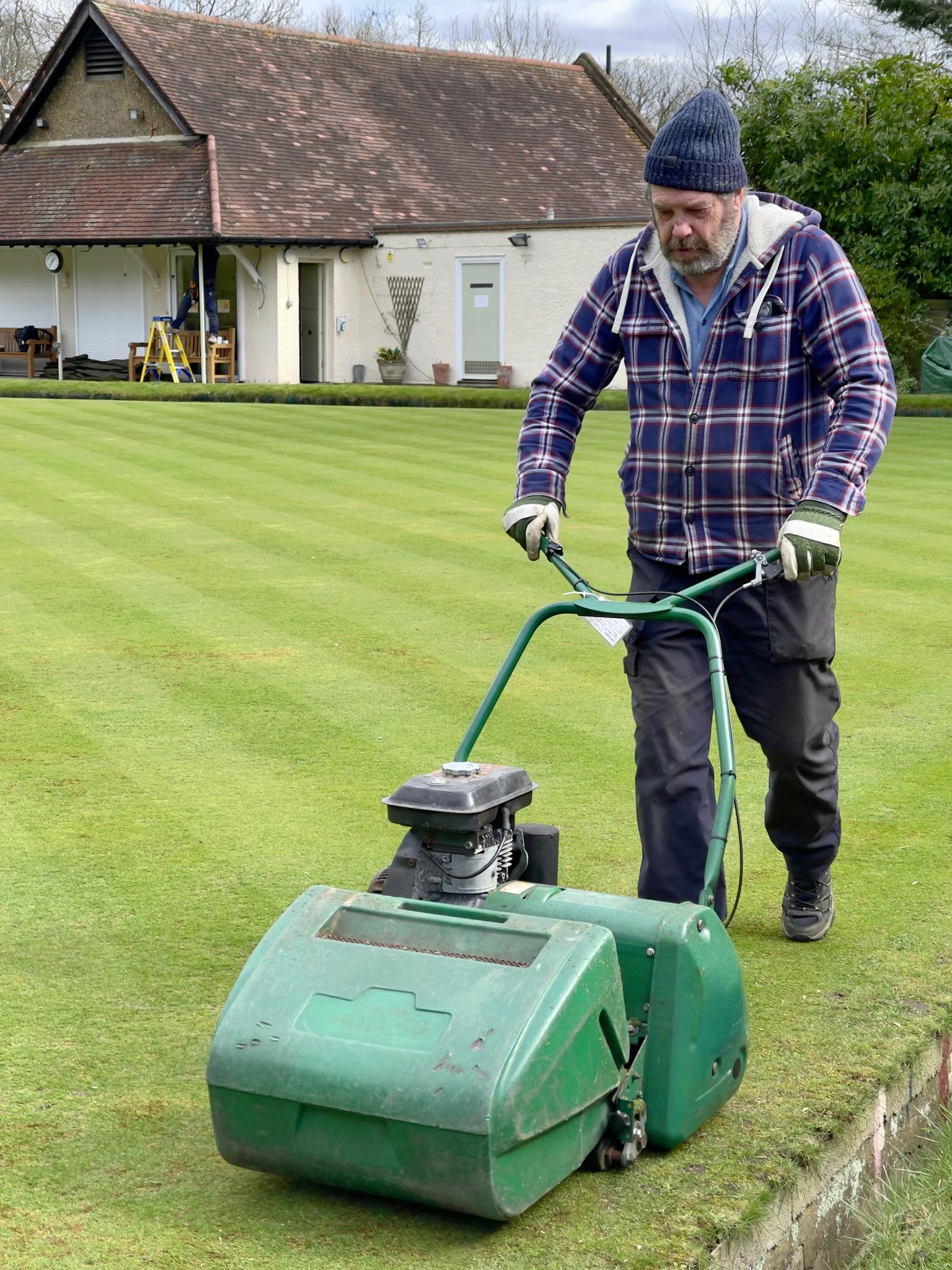 A man using a lawnmower to cut grass in a garden setting in Greater London.